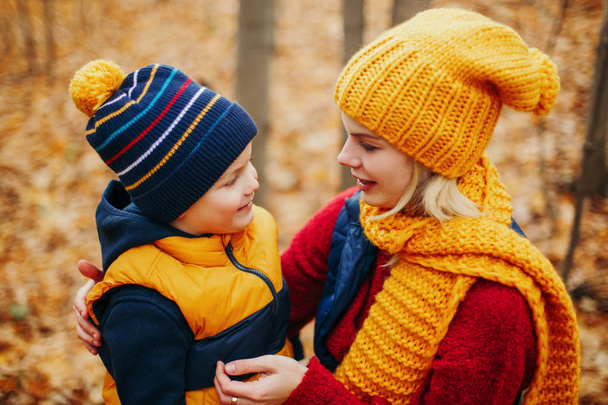 Caucasian young mother hugging talking to cute adorable toddler boy son in autumn fall park outdoor with yellow orange red tree leaves. Happy family. Autumnal seasonal activity outdoor. - Foto, immagini
