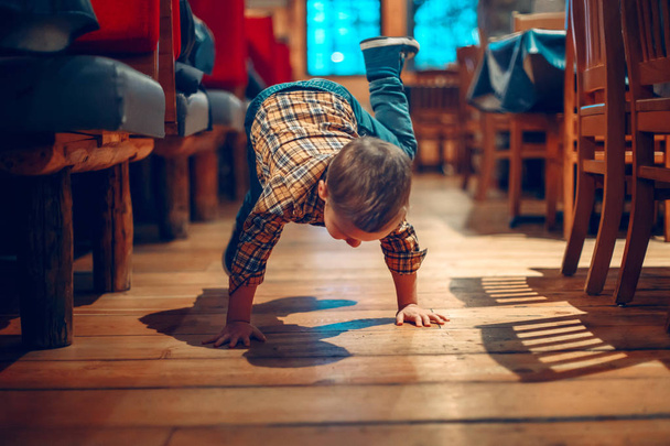 Cute adorable boy three years old having fun in cafe restaurant. Child playing on floor in public place. Freedom of self expression and behaviour for kids. Toddler touching dirty ground. - Photo, Image