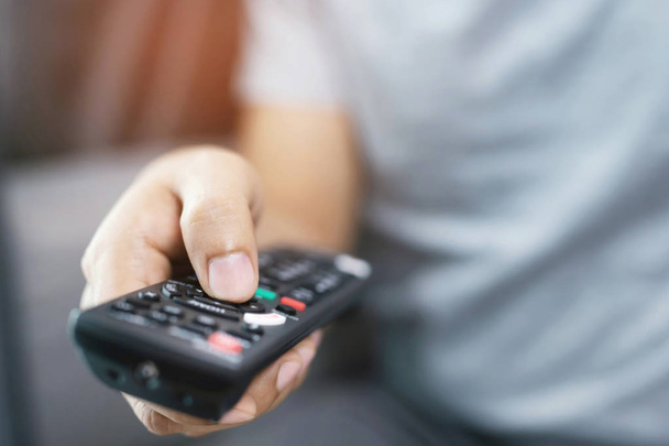 close up Television remote control in casual man hands pointing to tv set and turning it on or off. select channel watching tv on his sofa at home in the living room relax. - 写真・画像