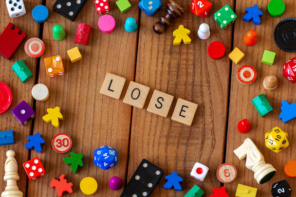 "lose "geschrieben in hölzernen Buchstaben Kacheln. umgeben von Würfeln, Karten und anderen Spielsteinen auf einem hölzernen Hintergrund - Foto, Bild