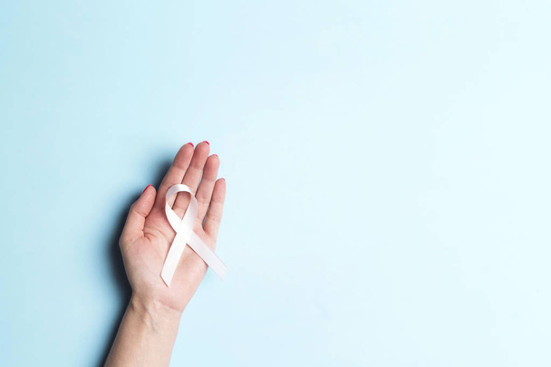 Female hand holding white ribbon on a blue background.  - Foto, afbeelding