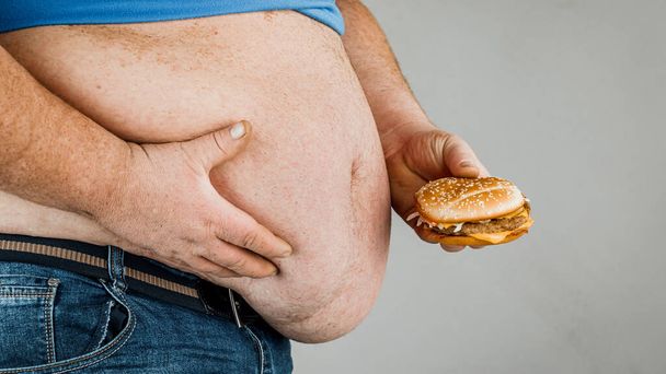 tlustý muž s hamburgerem v ruce na šedém pozadí. - Fotografie, Obrázek