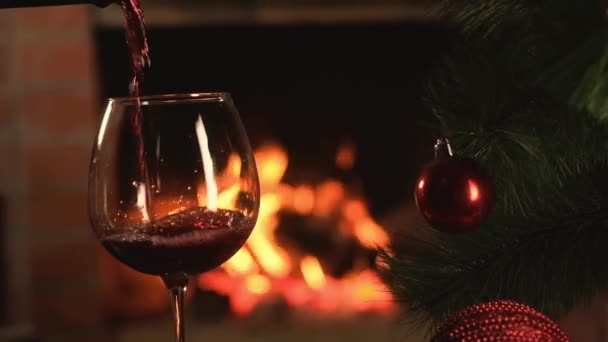 il vino rosso è versato in calice di vetro di vino chiaro su sfondo di fiamma ardente di camino di Natale. Albero di Natale artificiale con belle decorazioni. Vacanze di anno nuovo con famiglia
 - Filmati, video