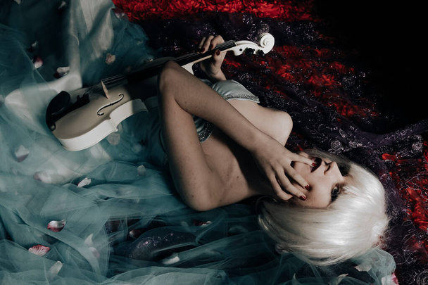 νεαρή ξανθιά γυναίκα με λευκή βιολέτα τη νύχτα ξαπλωμένη στο κρεβάτι - Φωτογραφία, εικόνα