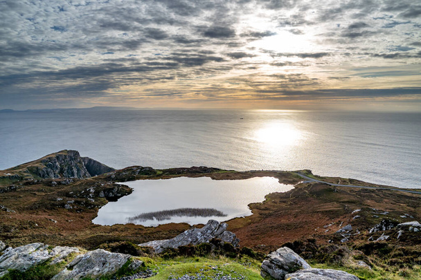 Zachód słońca nad jeziorem w Slieve League Cliffs, które należą do najwyższych morskich klifów w Europie wznoszących się 1972 stóp nad Oceanem Atlantyckim - hrabstwo Donegal, Irlandia. - Zdjęcie, obraz