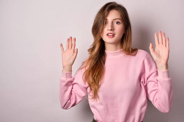 The girl in pink t-shirt standing on a light background, surprised mouth open looking at the camera, holding up his hands. - Фото, зображення