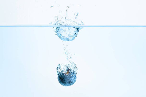 eine organische Blaubeere versinkt in Wasser mit Luftblasen weißem Hintergrund. Makro-Detailaufnahme. - Foto, Bild