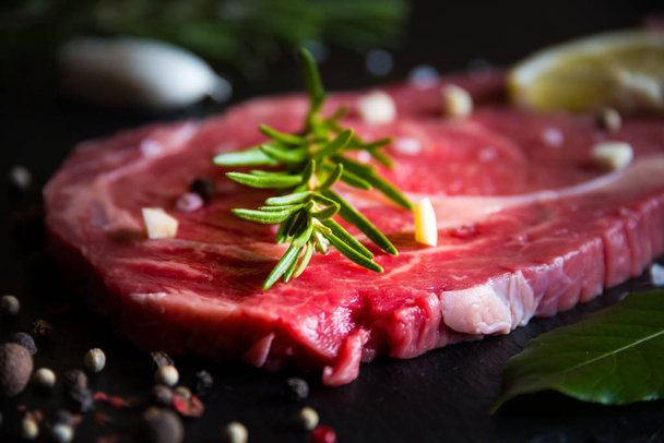 Raw beef meat, uncooked steak with rosemary, lemon and spices on black - Valokuva, kuva