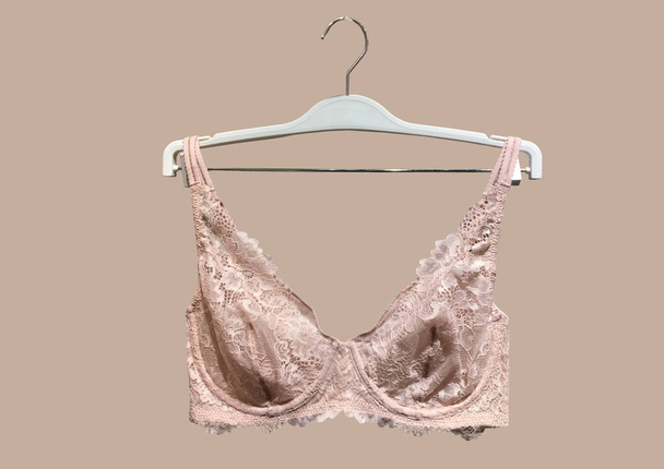 Lace bra on a hanger isolated on brown background. Textile, Underwear. Vintage White Lace Bra unlined lace detailing. Sexuality and seductive lingerie. Fashion concept. Stylish lingerie - Foto, imagen