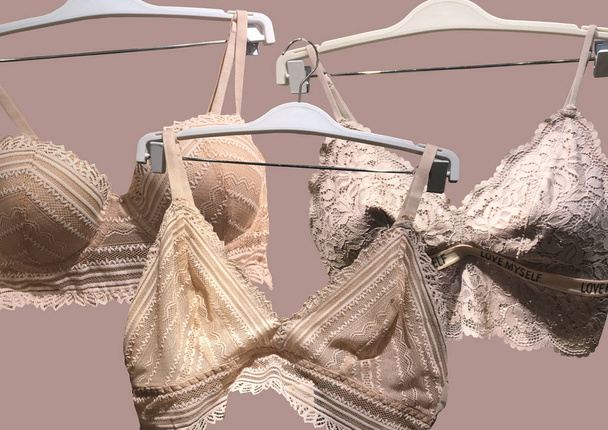 Lace bras on a hanger isolated on brown background. Textile, Underwear. Vintage White Lace Bras unlined lace detailing. Sexuality lingerie. Fashion concept. Stylish lingerie. Set of female underwear - Photo, Image