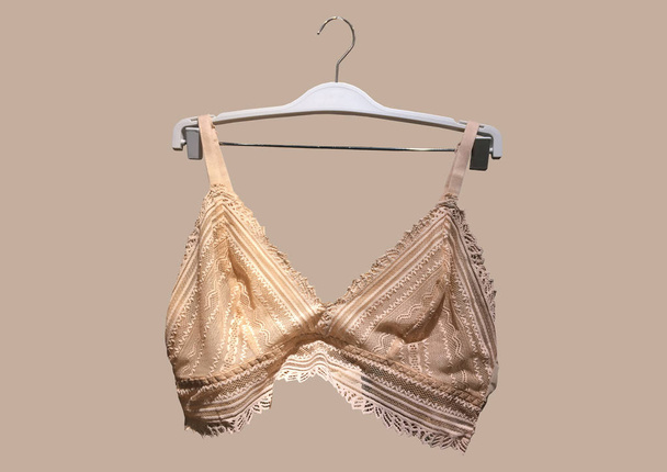 Lace bra on a hanger isolated on brown background. Textile, Underwear. Vintage White Lace Bra unlined lace detailing. Sexuality and seductive lingerie. Fashion concept. Stylish lingerie - Photo, Image