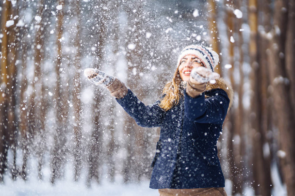 Happy young woman plays with a snow in sunny winter day. Girl enjoys winter, frosty day.  Playing with snow on winter holidays, a woman throws white, loose snow into the air. Walk in winter forest. - Foto, Imagem