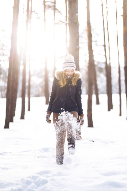 Happy young woman plays with a snow in sunny winter day. Girl enjoys winter, frosty day.  Playing with snow on winter holidays, a woman throws white, loose snow into the air. Walk in winter forest. - Photo, image