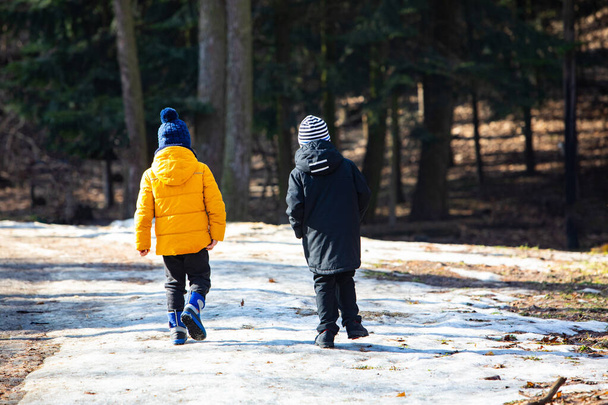 Két téli ruhás fiú sétál a havas park mellett - Fotó, kép