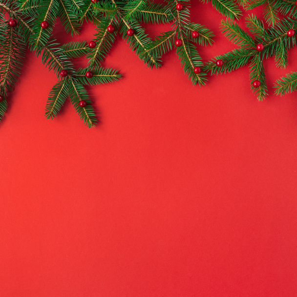 Composición de Navidad / Año Nuevo. Ramas de abeto con bayas rojas sobre fondo rojo. Plano laico, vista superior concepto festivo creativo
. - Foto, Imagen