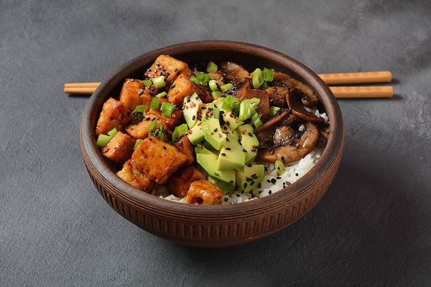Sweet, spicy , crispy and fried Tofu in teriyaki sauce served in a bowl with avocado,fried mushrooms, sesame seeds and rice. Healthy vegan food, gluten-free - Φωτογραφία, εικόνα