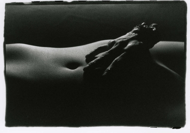 On a tender naked female tummy lies a torn human hand. - Фото, зображення