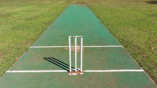 Scenic cricket ondergrond astro tapijt slagveld met witte grens hek van gras veld ochtend zomer blauwe dag landschap. - Foto, afbeelding