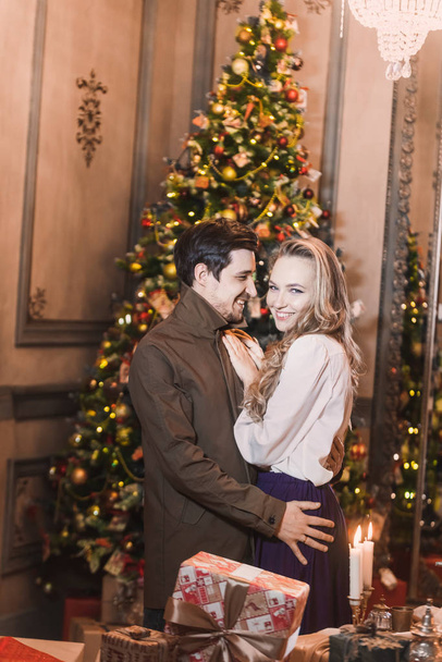 couple of beautiful young  blonde girl her boyfriend on background merry Christmas happy new year tree lights with star gift decor. Family shooting - 写真・画像