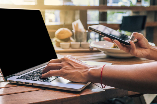 Mãos de mulher segurando um telefone inteligente e digitando em um laptop com branco
. - Foto, Imagem