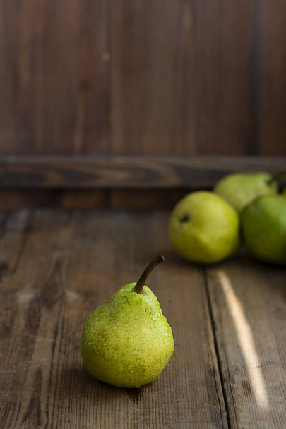 one fresh ripe organic yellow pear on rustic wooden brown table with defocused pears on background. Selective focus. Vertical with copy space. For design about agricilture, fruit and healthy food - Foto, Bild