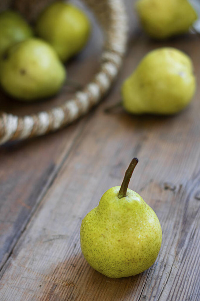 fresh green pear on rustic wooden brown table with defocused pears in basket on background. Selective focus. Vertical. For design and postcard about agricilture, fruit, healthy food, vegan - Foto, Bild