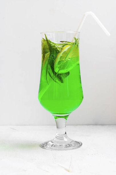 Summer cold green drink made from tarragon, with mint and slices lemon in glass with straw on light background. Sparkling beverage, lemonade. Horizontal with copy space - Φωτογραφία, εικόνα