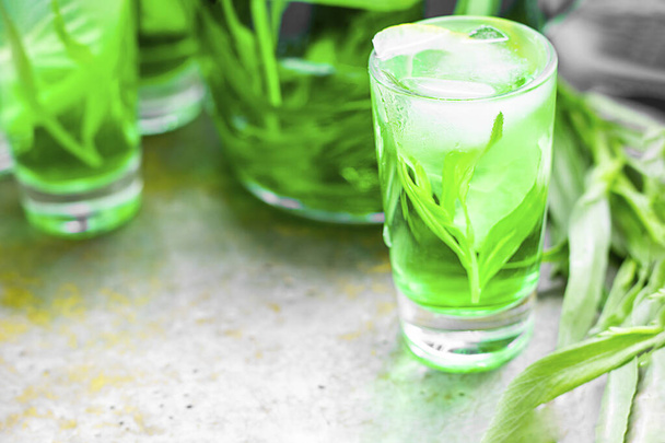 Summer cold green drink with tarragon, mint and lemon in small shot with ice and defocused decanter on background. Sparkling beverage, alcohol drink on dark background. Horizontal, copy space - Foto, immagini