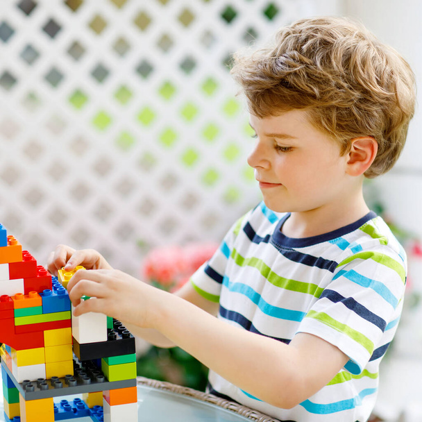 Little blond child playing with lots of colorful plastic blocks. Adorable preschool kid boy wearing colorful shirt and having fun with building big castle and creating a house - Photo, Image