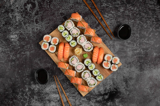 Sushi preparado para dois. Nigiri e maki rolos servidos em tábua de madeira sobre fundo de pedra escura. Comida japonesa. Vista superior
 - Foto, Imagem