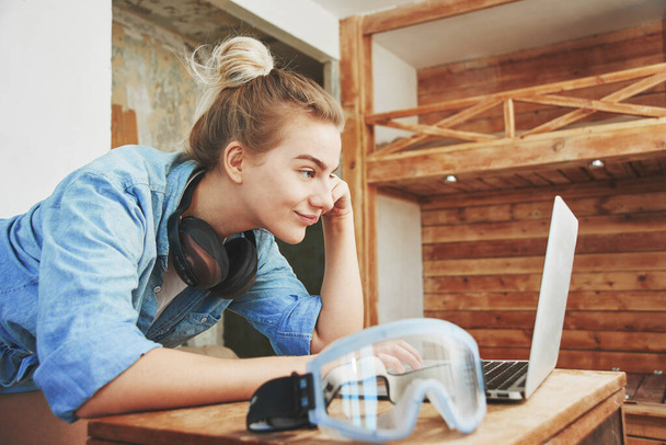 Happy young woman in construction clothes with laptop plans and makes repairs on the background of homemade wooden bunk bed, DIY concept - Fotó, kép