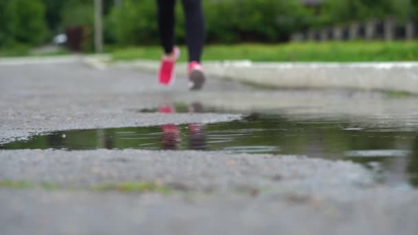 スニーカーのランナーの足。スポーツウーマンは屋外でジョギングをし、泥だらけの水たまりに足を踏み入れる。雨の中を走るシングルランナーが飛び散る。スローモーション - 映像、動画