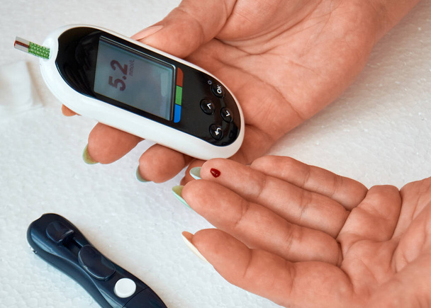 A diabetic checks his blood sugar. The woman is self-tested with a Lancet and a glucometer at home. - Foto, afbeelding