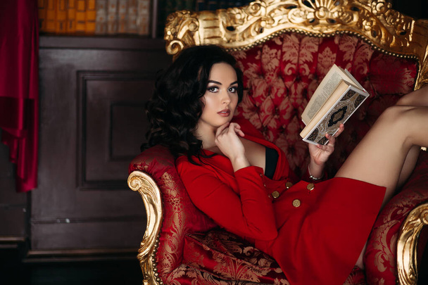 Menina quente em curto vestido vermelho segurando livro, deitado na biblioteca
. - Foto, Imagem