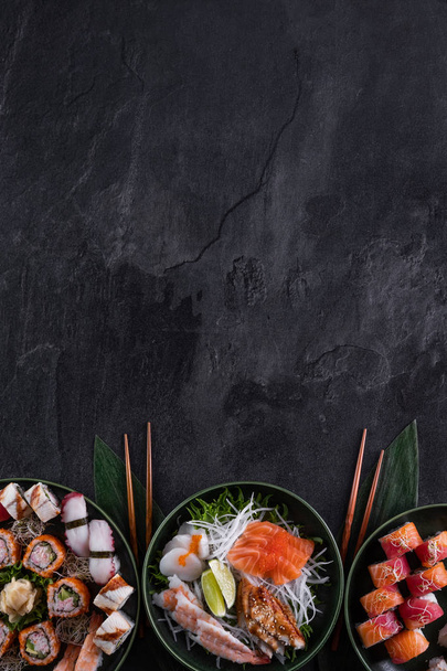 Surtido de sushi sobre fondo de pizarra oscura. Rollo de sushi maki con salmón, vieira, anguila y sashimi de camarón servido con rábano daikon. Copia espacio para texto. Menú del restaurante. Comida tradicional japonesa
. - Foto, Imagen
