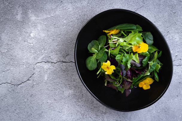 Salad bowl with greens, vegetables and flowers on grey stone background. Tasty, healthy, vegan food. Top view with copy space - Fotoğraf, Görsel