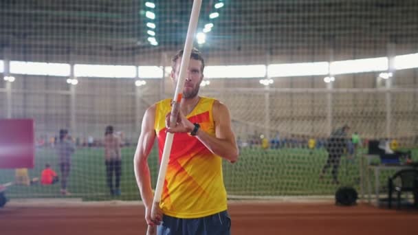 Pole vaulting indoors - a man in yellow shirt standing on the track with a pole - take deep breaths and starts running - Footage, Video