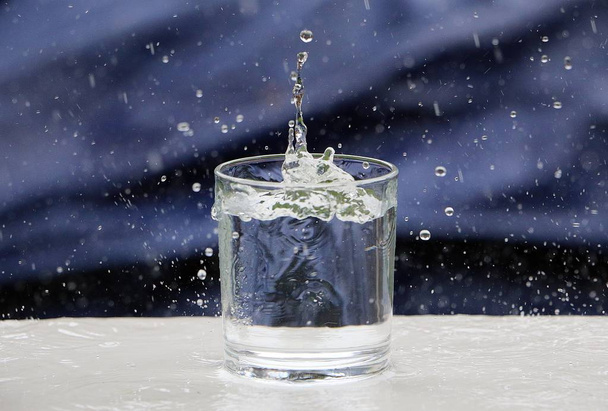 gouttes de pluie tombent dans un verre d'eau qui se tient sur la table dans le jardin
 - Photo, image