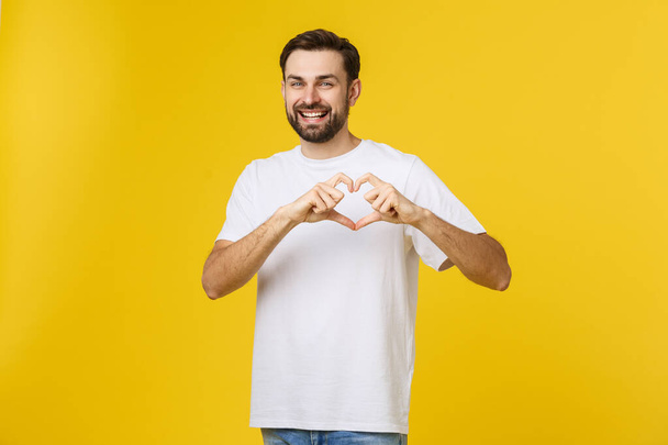smiling young boy making heart gesture on his chest with white shirt isolated on yellow background - Photo, Image