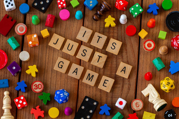 "Je to jen hra "napsaná v dřevěných dlaždicích. Obklopen kostkami, kartami a dalšími herními figurkami na dřevěném pozadí - Fotografie, Obrázek