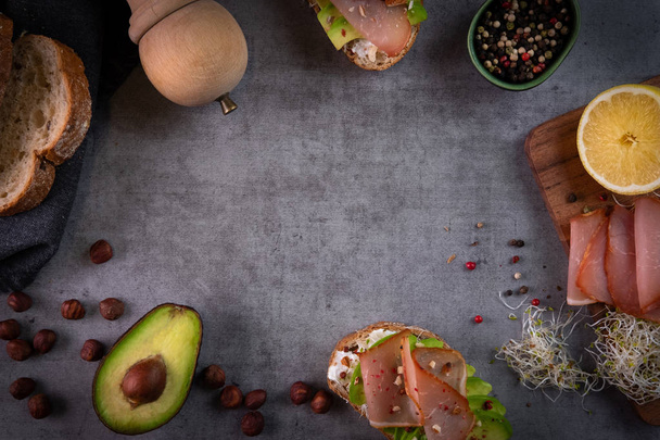 Делать бутерброды с авокадо плоским слоем на темно-сером каменном фоне. Здоровый завтрак, концепция здорового питания. Авокадо тост с козьим сыром, орехами, капустой, ветчиной и специями. Вид сверху, пространство для копирования
 - Фото, изображение