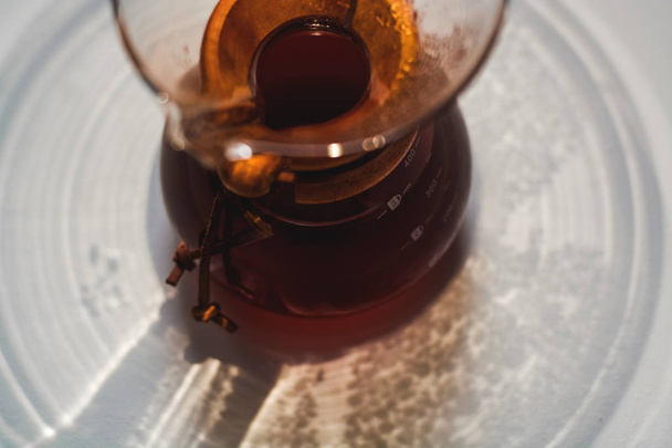 Glasbehälter gefüllt mit schwarzem Kaffee auf einer Tonne weißem Hintergrund mit Reflexion großer und ungewöhnlicher Schatten. - Foto, Bild