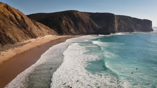 Un drone aérien d'une vague frappant une plage à côté d'une chaîne de montagnes où les gens nagent et surfent en Algarve, Portugal
. - Séquence, vidéo