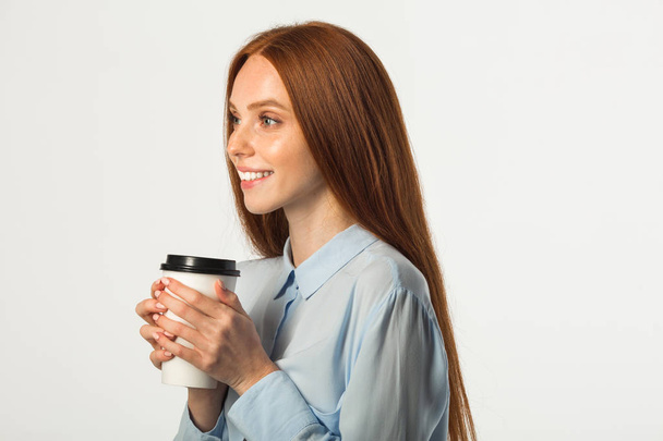 όμορφη νεαρή γυναίκα με κόκκινα μαλλιά με ένα ποτό στο χέρι σε λευκό φόντο - Φωτογραφία, εικόνα