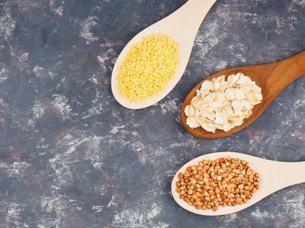 Groats buckwheat, oatmeal, millet in wooden spoons on a dark con - Foto, Imagem