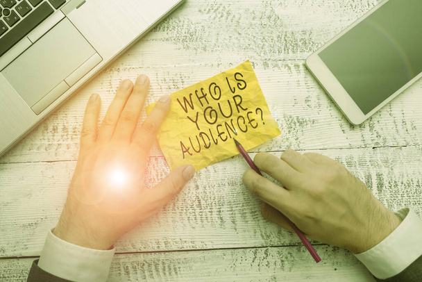 Text sign showing Who Is Your Audience Question. Conceptual photo who is watching or listening to it Hand hold note paper near writing equipment and modern smartphone device. - Photo, Image