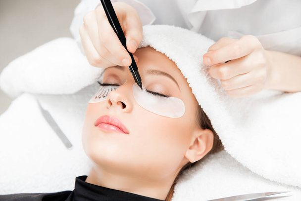 Eyelash extension procedure. Master tweezers sets fake lashes on beautiful woman - Photo, Image