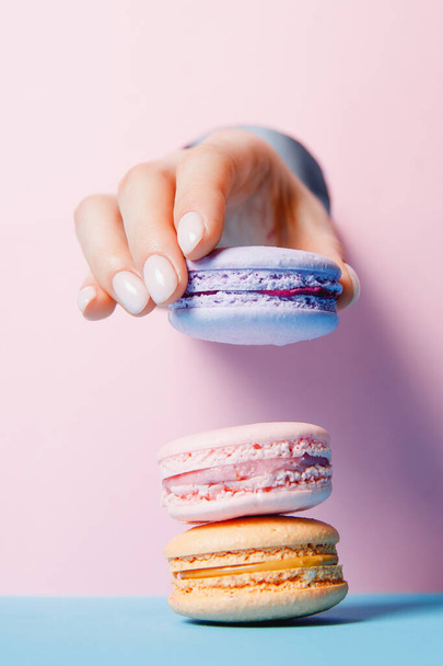 Beautiful girl hands with trendy manicure nail holding color macaroon cake through hole in pink background - Foto, Imagem