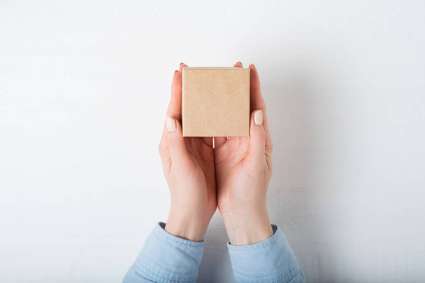 Pequeña caja cuadrada de cartón en manos femeninas. Vista superior, fondo blanco
 - Foto, Imagen