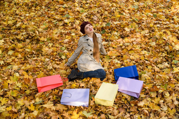 Щаслива молода жінка сидить з кольоровими пакетами на листі. Шопінг. Осінній день
 - Фото, зображення